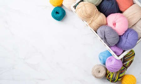 pastel colored yarn wool in a white basket on marble background