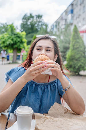 Summer vacation, street food eating. closeup of woman hands holding hamburger, woman eating fast food at street cafeの写真素材