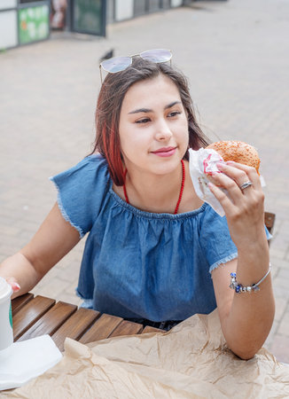 Summer vacation, street food eating. closeup of woman hands holding hamburger, woman eating fast...
