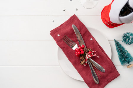 Christmas table setting with white dishware, silverware and red and green decorations on white...