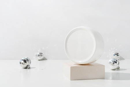 A minimalistic scene of plastic cream box on podium with christmas decorative balls on light background. Showcase with a stage for products, mockup design, seasonalの写真素材