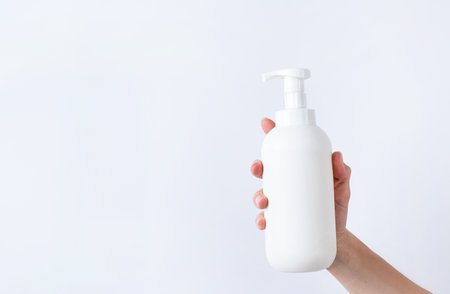 Woman hand holding blank white plastic container in light gray background. Cosmetic beauty product branding mockup. copy spaceの写真素材