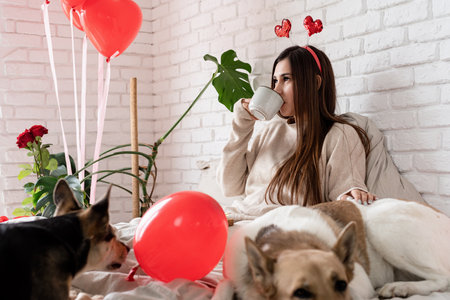 Valentine's day, Women's day. Young beautiful brunette woman sitting in the bed with her dog celebrating valentine day, eating sweets and drinking coffeeの写真素材