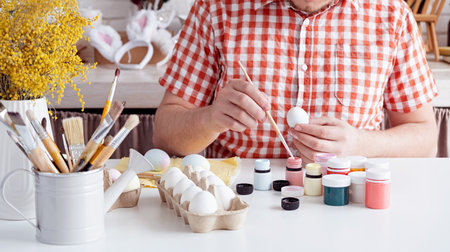 Spring holidays, Easter. Man in plain shirt painting easter eggs at home kitchenの写真素材