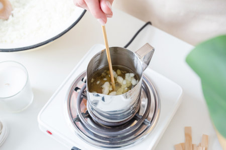 creative hobby at home. Woman making decorative aroma candles at table, melting soy wax in metal pitcher or jugの写真素材