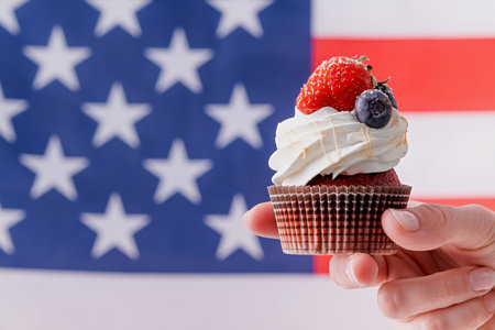 Fourth of july celebration. hand holding sweet cupcake with blueberries and strawberry , flag backgroundの写真素材