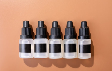 Set of plastic dropper bottles with liquid with black blank stickers. Mockup on brown background...