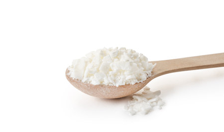 Organic white soy wax flakes for candles in small measure spoon isolated on white background with...