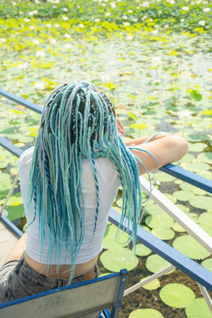 young beautiful woman with blue afro locks resting on lotus lake enjoying nature