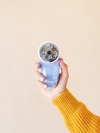 Device for shaving pellets clothes. Anti-Plush Fabric Shaver. Electric portable sweater pill defuzzer. hand holding device and beige backgroundの写真素材