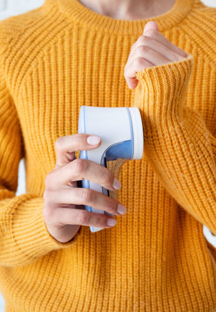 woman uses a machine for removing pellet and spools from clothes and fabric on yellow sweater. A...
