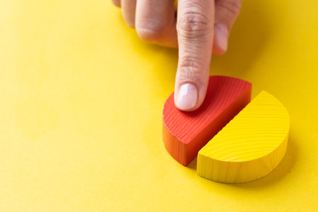 Colorful wooden pie chart pieces on bright yellow background with copy space, finger adding piece of chartの写真素材