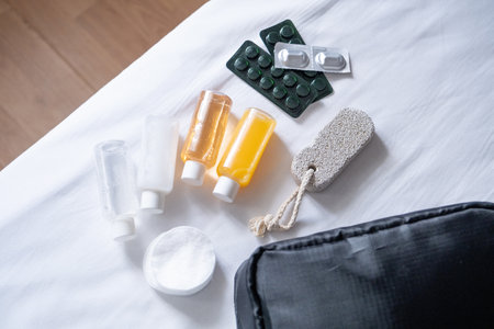 Travel cosmetics kit with bottles, pills and cosmetics on bed, top view