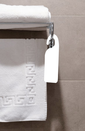 Set of white towels in the bathroom of a hotel room hung on a hanger with blank tag for mockupの写真素材