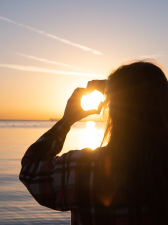 hands forming a heart shape with sunset silhouette on the beachの写真素材