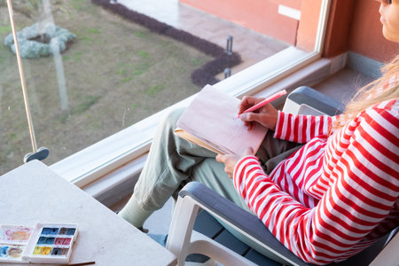Draw in sketchbook. back view of a woman sketching in sketchbook sitting on the balconyの写真素材