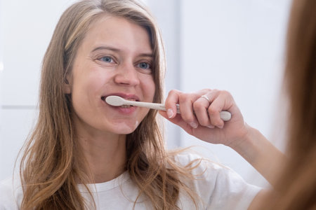 morning routines. Young woman brushing her teeth at mirror