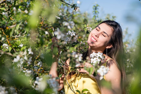 Spring concept. Nature. Young caucasian woman wearing yellow dress enjoying the flowering of an apple trees, walking in spring apple gardensの写真素材