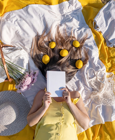 Spring concept. Nature. Young caucasian woman wearing yellow dress, having a picnic, lemons in hairの写真素材