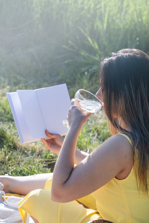 Spring concept. Nature. Young caucasian woman wearing yellow dress enjoying the flowering of an apple trees, having a picnic and reading bookの写真素材