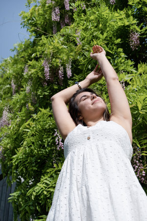 woman in a blooming wisteria garden, around flowers. The girl holds a branch of lilac flowers in her...
