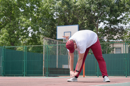 Athletic bearded man wearing red pants and cap warms up before workout at the stadium. Space for textの写真素材
