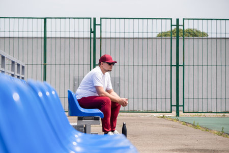 sportsman wearing red sports clothes with a bottle of water sitting and resting at the seats at the stadiumの写真素材