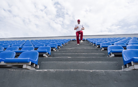 sportsman wearing read and white sport clothes running in the stadium among blue seatsの写真素材