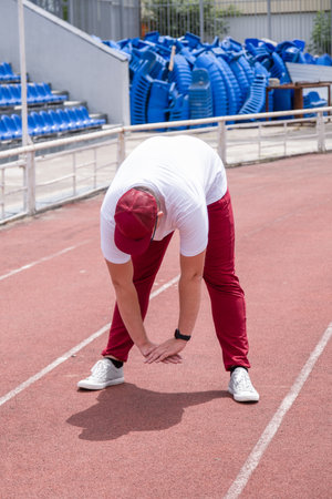 Athletic bearded man wearing red pants and cap warms up before workout at the stadium. Space for textの写真素材
