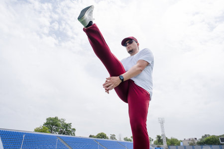 Athletic bearded man wearing red pants and cap warms up before workout at the stadium. Space for textの写真素材