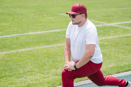 Athletic bearded man wearing red pants and cap warms up before workout at the stadium. Space for textの写真素材