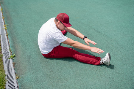 Athletic bearded man wearing red pants and cap warms up before workout at the stadium. Space for textの写真素材
