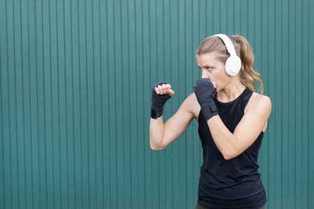 young sportive blond female boxer training, ready to punch, green wall backgroundの写真素材
