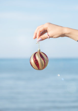 celebrating Christmas in hot countries. hand holding colorful Christmas ball over blue sea and beach background, copy spaceの写真素材