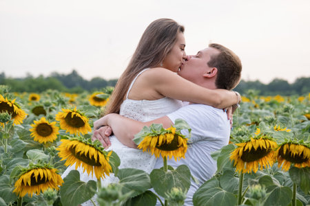 Cheerful couple kissing amidst sunflowers in field at sunsetの写真素材