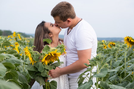 Cheerful couple amidst sunflowers in field at sunsetの写真素材