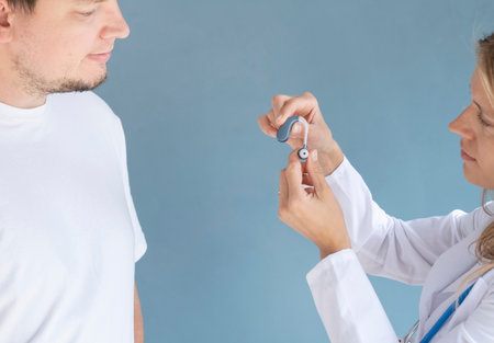 young male patient testing hearing aid in clinic exam room, young female doctor helpingの写真素材