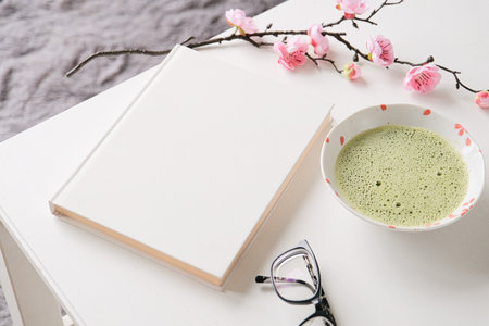 blank book mockup on white wooden coffee table with green matcha tea, sakura branch and glasses, Asian styleの写真素材