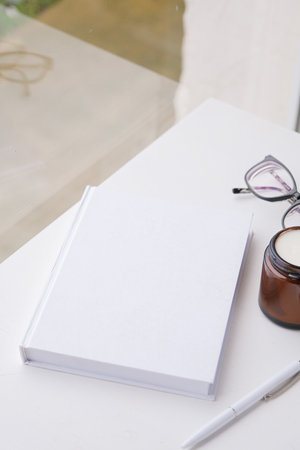 blank book mockup on white wooden coffee table with candles near window, Asian style