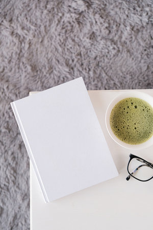 blank book mockup on white wooden coffee table with green matcha tea near window, Asian styleの写真素材
