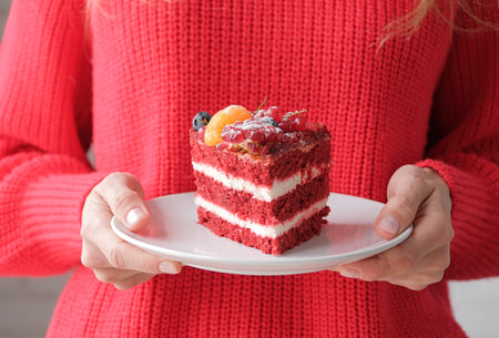 woman wearing red sweater holding piece of red velvet cake with fruit