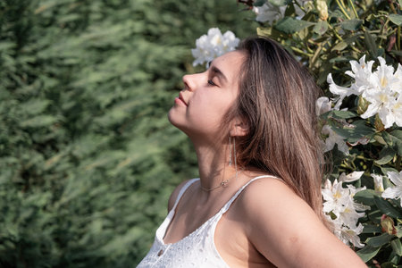 Spring blossom. beautiful young woman wearing white summer dress surrounded by white rhododendron...