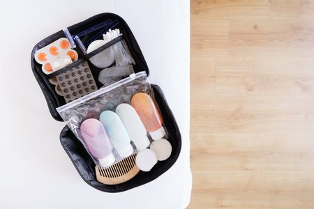Black cosmetic travel kit on the bed. colorful cosmetic bottles packed in plastic bag, pills and hygiene items for travel, blurred wooden floorの写真素材