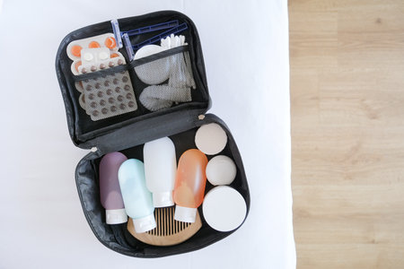Black cosmetic travel kit on the bed. colorful cosmetic bottles, pills and hygiene items for travel,...