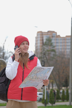 Vibrant female tourist woman holding map exploring new city and talking on the phone, looking around...