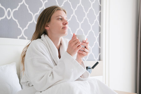 Relaxed woman holding mug of hot beverage on bed in the hotel roomの写真素材