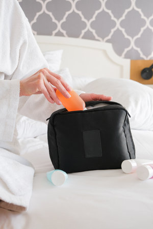 woman hands holding cosmetic travel kit on the bed. colorful cosmetic bottles and hygiene items for travelの写真素材