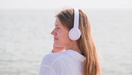 Woman wearing headphones listening to music breathing fresh air relaxing walking on the beachの写真素材
