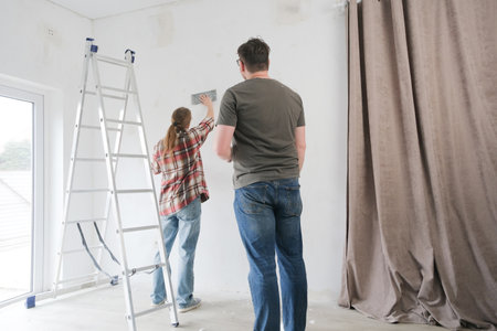 Happy couple renovating new house apartment. Home makeover, renovation concept. Processing of a wall by an sandpaper, vertical videoの写真素材