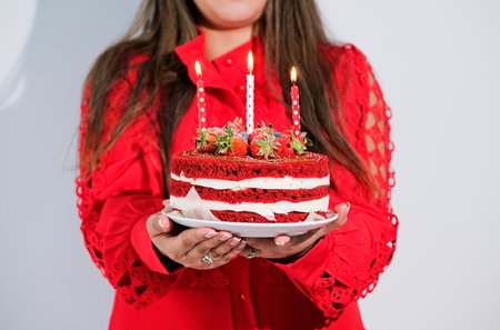 cheerful woman wearing red dress celebrating birthday and lighting candles on red velvet cake. Holiday Celebration, Joyful Events Conceptの写真素材